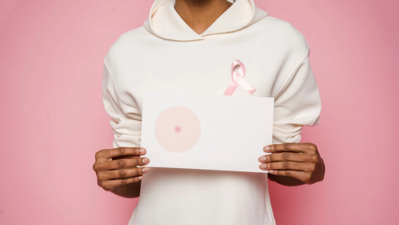 Vrouw met borstkanker heeft een roze lint opgespeld en houdt een papier vast waar een borst op is getekend.