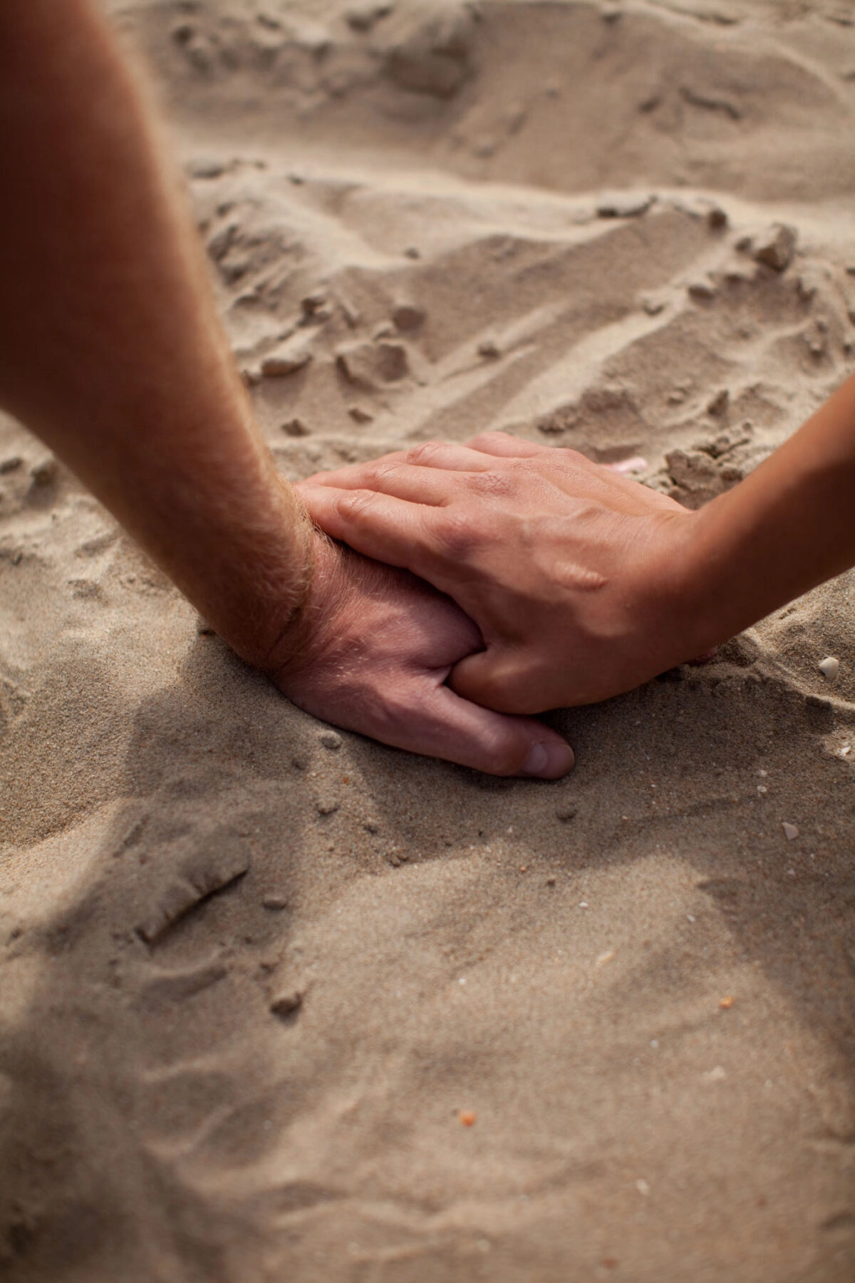 Twee handen houden elkaar vast op het strand.