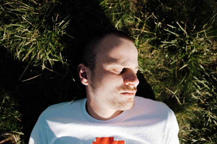 Een man ligt in het gras met angstklachten bij kanker.