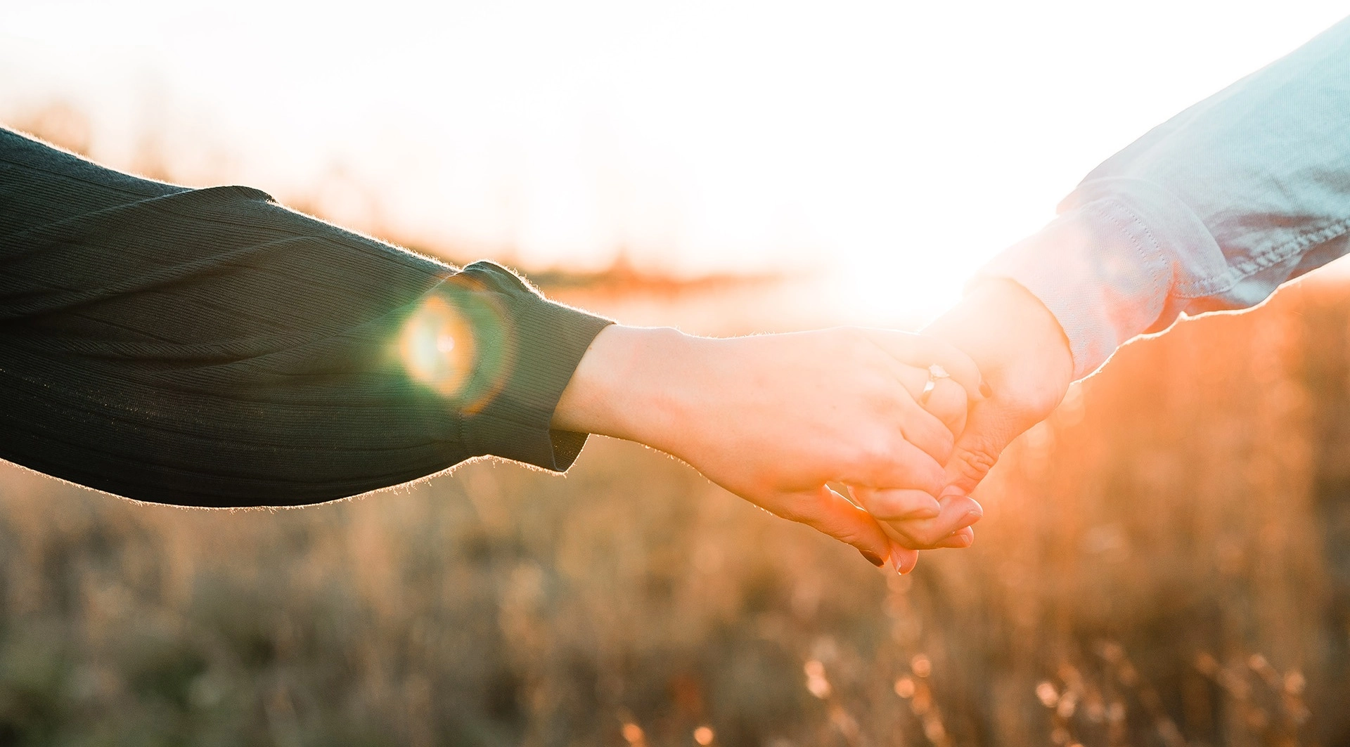 Twee mensen in relatietherapie houden elkaars handen vast in een veld.