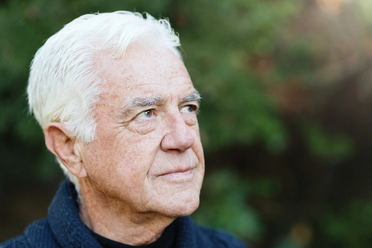 Senior man outdoors in garden looks uncertainly into the metaphorical future