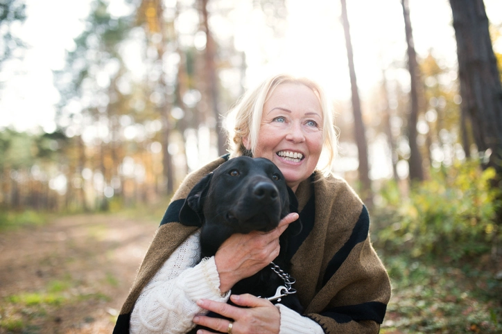 A portrait of a happy senior woman with a dog in autumn nature.